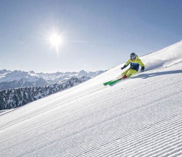Skifahrer fährt rasant eine frisch präparierte Skipiste herunter, die Sonne scheint an einem wolkenlosen Himmel. © Silvretta-Montafon - Michael Müller