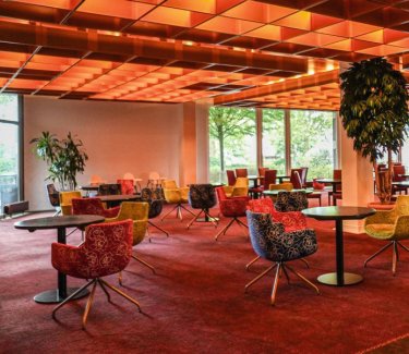 Großer Raum in Orangetönen runden Tischen und Sesseln. © Hotel Bettenburg Hamburg-Nettelnburg