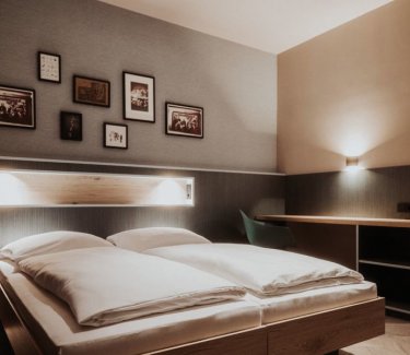 Doppelbett vor dunkelbraune Wand mit mehreren Bildern in Rahmen. © Schulz Hotels