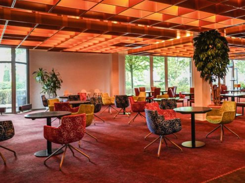 Großer Raum in Orangetönen runden Tischen und Sesseln. © Hotel Bettenburg Hamburg-Nettelnburg