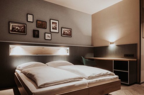Doppelbett vor dunkelbraune Wand mit mehreren Bildern in Rahmen. © Schulz Hotels